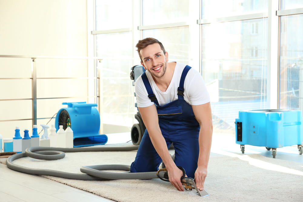 Person dress in blue smiling to camera while cleaning carpet for end of lease services