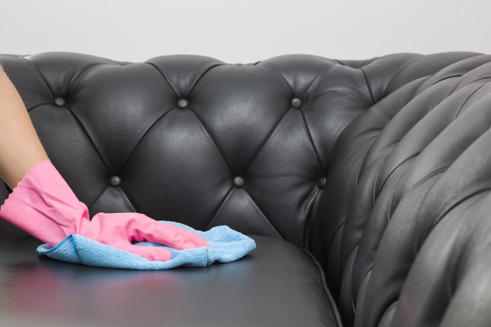 Picture of a hand with a glove cleaning upholstery leather couch with a cloth