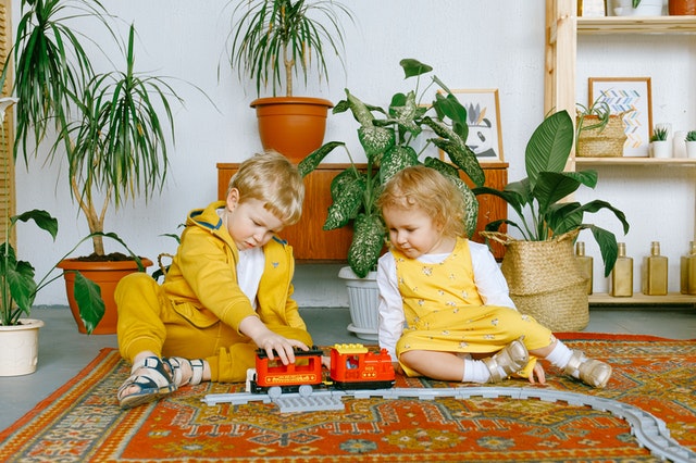 Two kids dress in yellow playing with a toy train. They are sitting on a rug that has been steam cleaned hours ago.