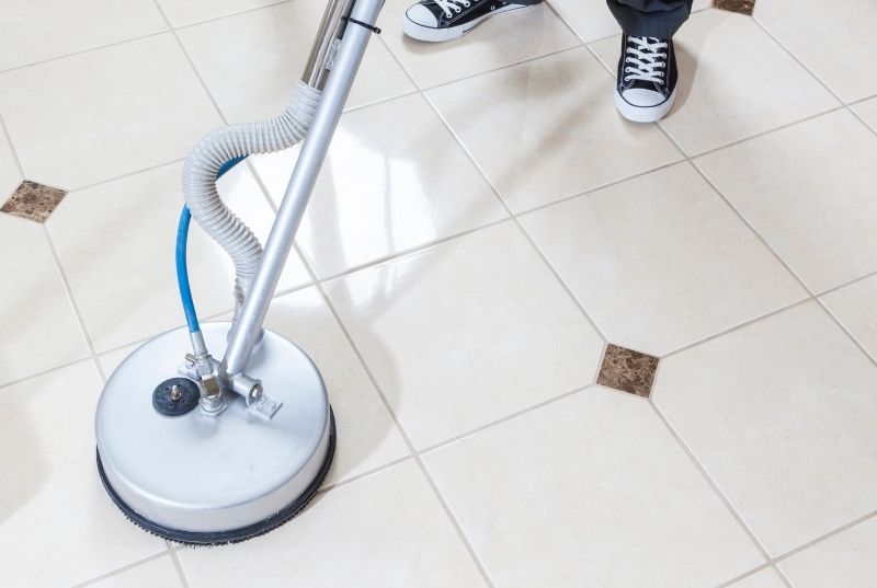 person using a tile cleaning hire machine on a white ceramic tile floor