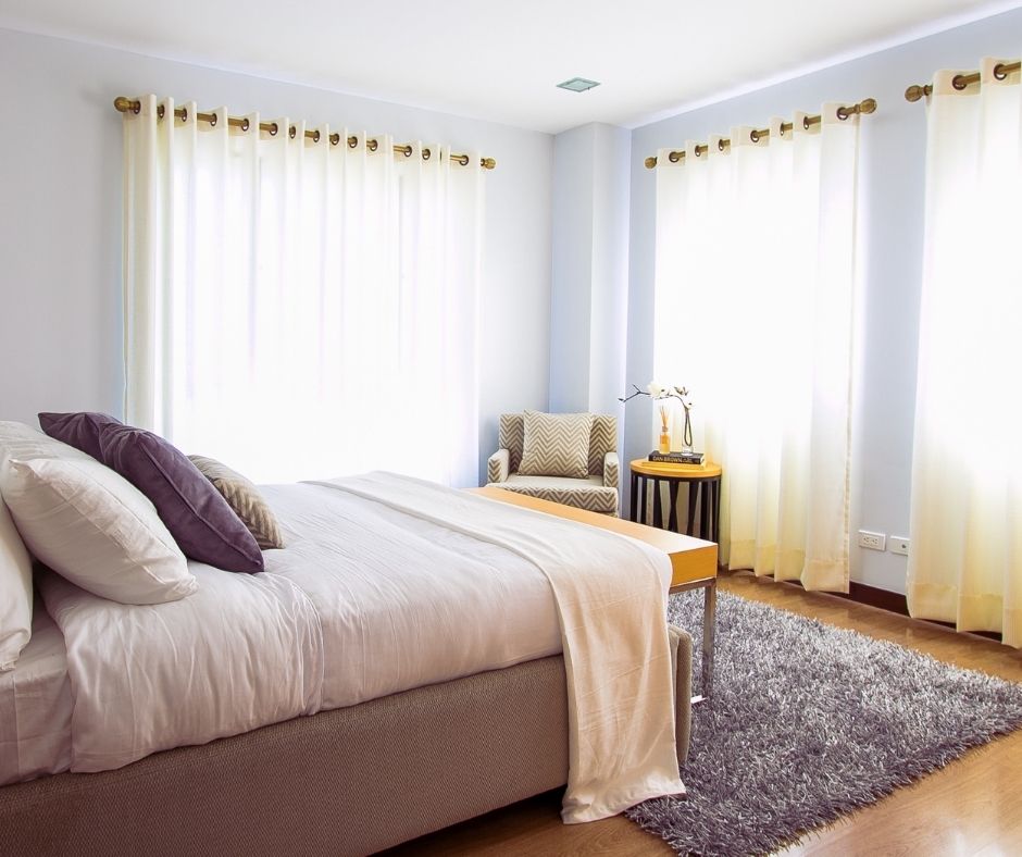 Bright bedroom with a bed and rug beside hardwood flooring