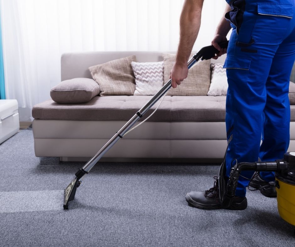 Man using a canister vacuum to clean a carpet next to a couch